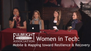 women at a roundtable discussion; one woman with a mic in her hand speaking; text overlay says "Women in Tech"