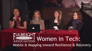 women sitting at a table for a roundtable discussion ; one woman is holding a mic. Text says "Women in Tech"