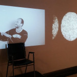 Some Collisions installation - 2 screens - 1 screen of person being interviewed and the other of metal compound